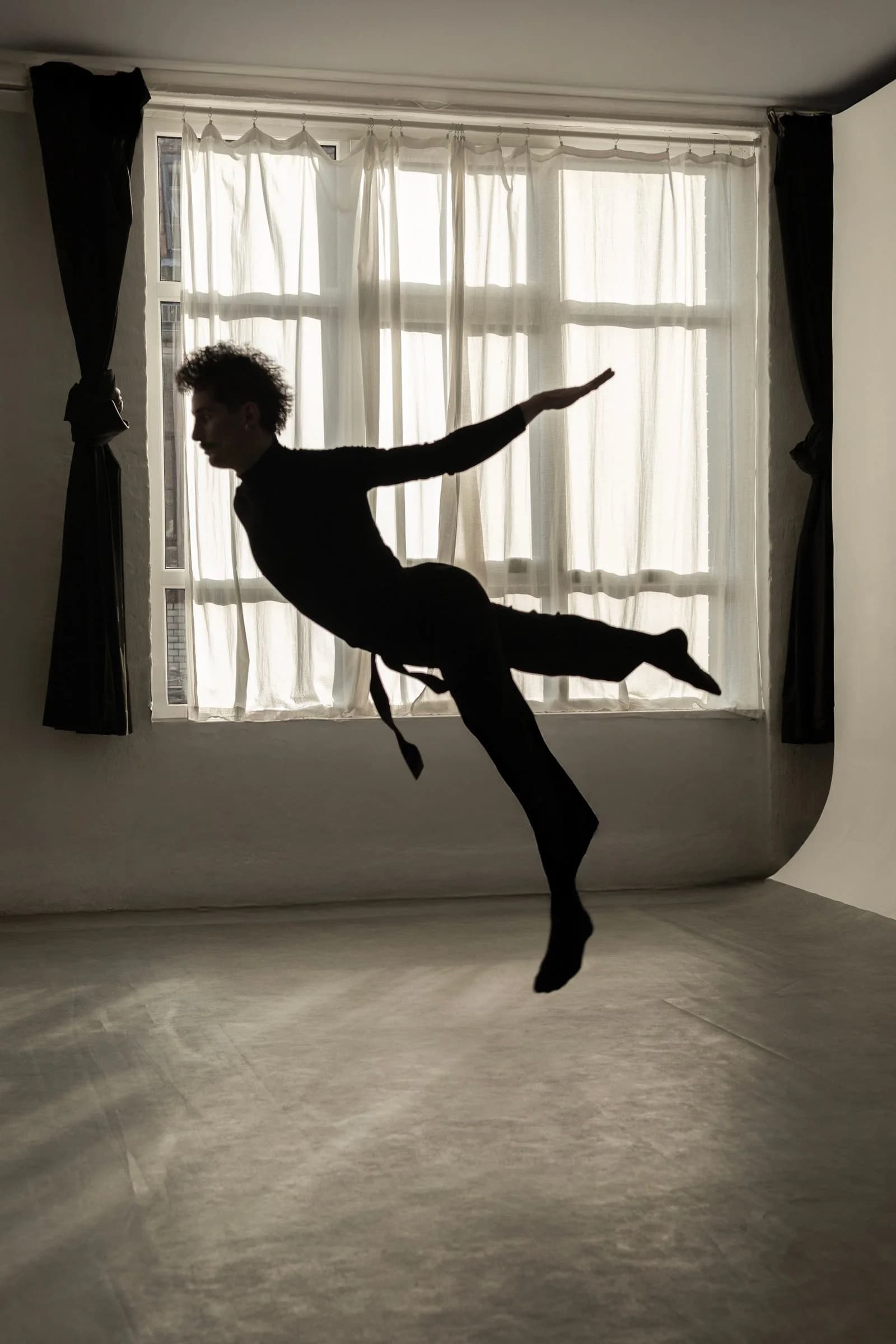 Dancer captured mid-leap in the light of a studio window